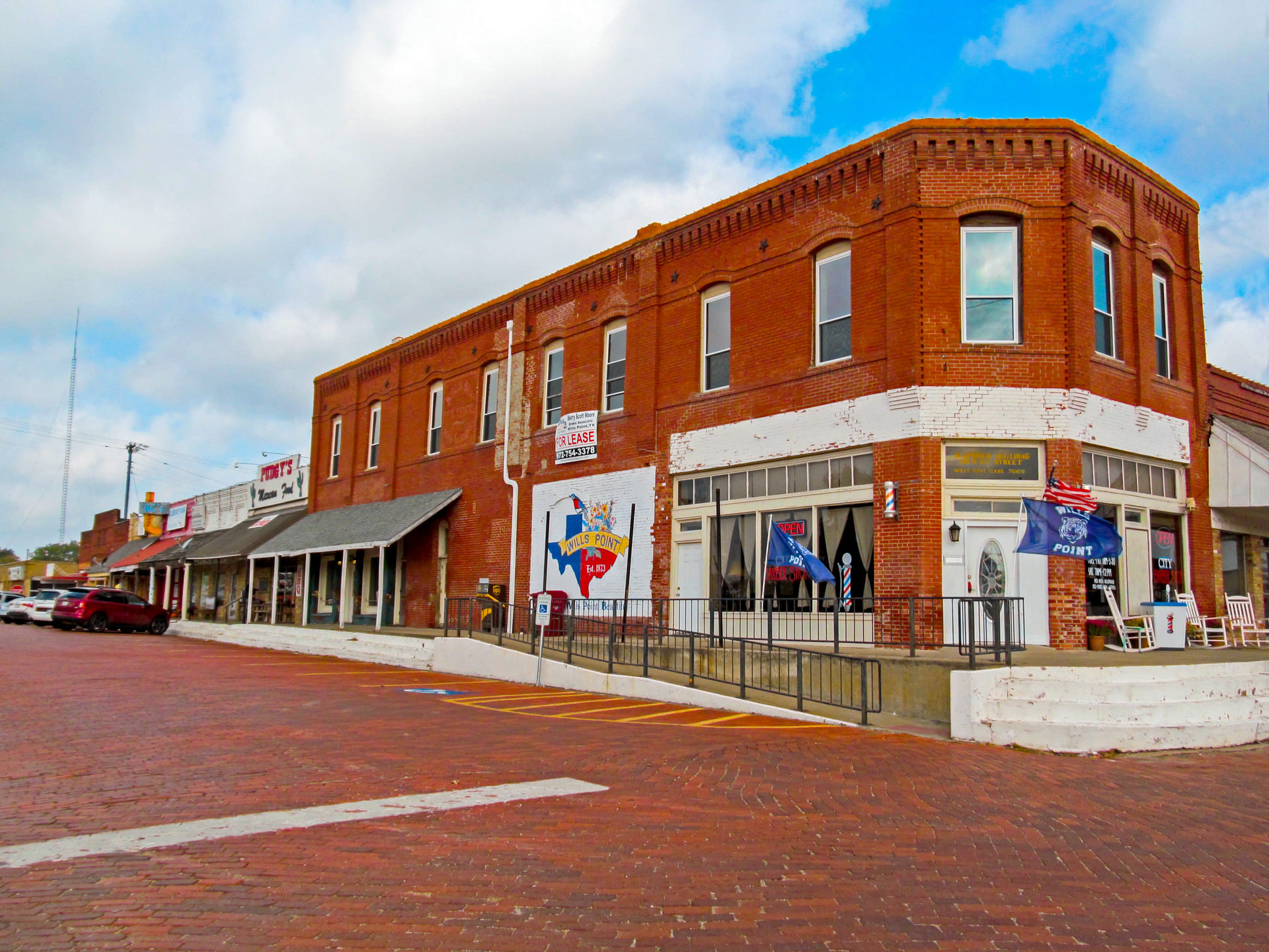 Historic downtown Wills Point, Texas featuring red-brick buildings, local shops, and a barbershop with American flags and Texas-themed murals.