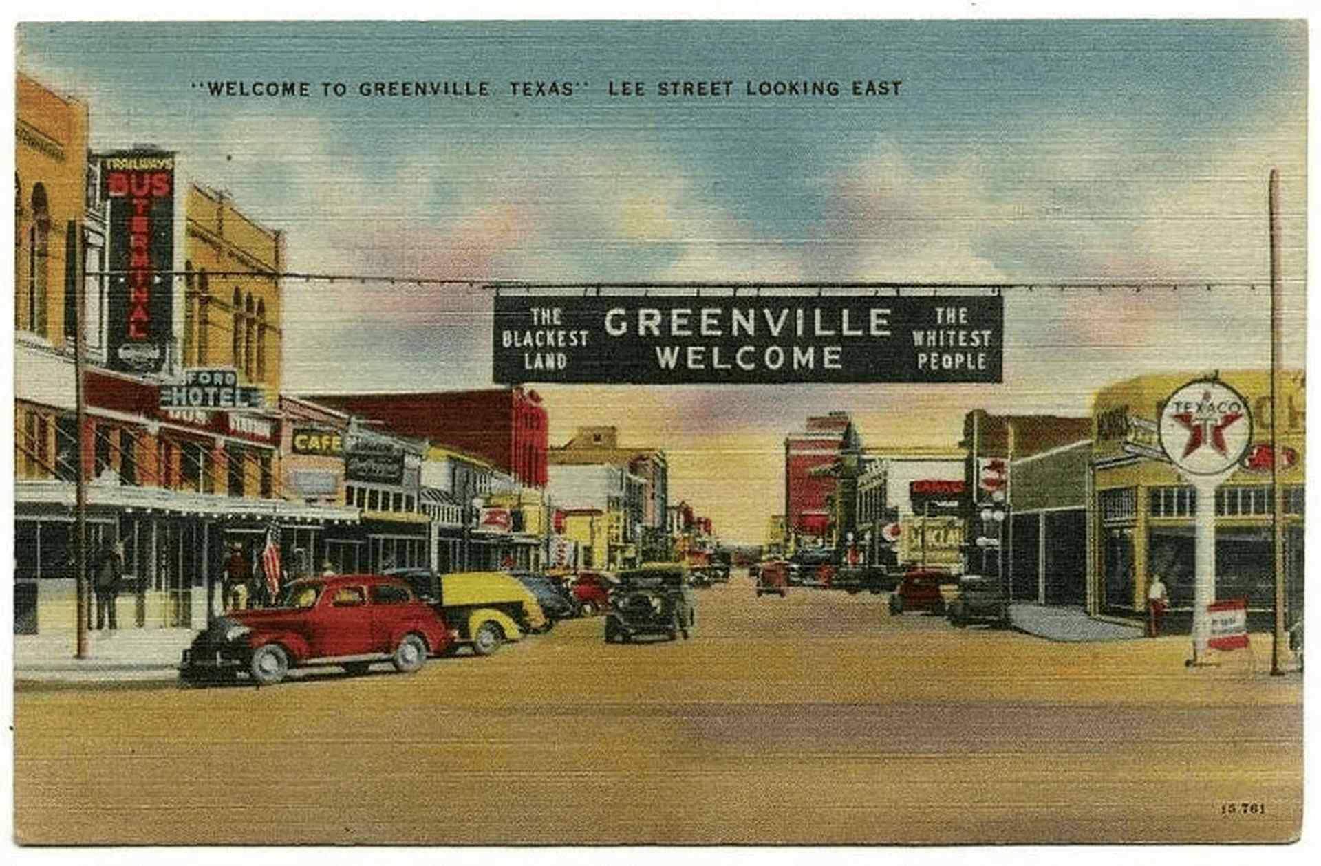 Vintage postcard view of downtown Greenville, Texas, showing a historic main street with classic storefronts, parked cars, and an overhead welcome banner spanning the road.