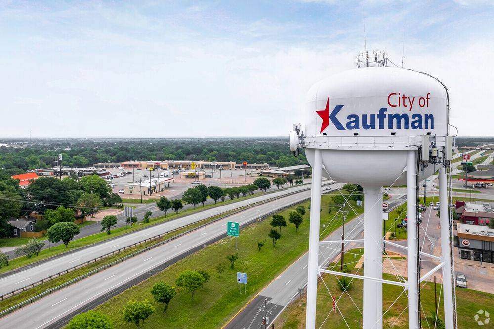 Aerial view of Kaufman, Texas, featuring the city water tower overlooking a major roadway, commercial businesses, and surrounding green landscape.