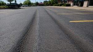 Severe asphalt rutting in a commercial parking lot, showing deep wheel-path depressions caused by heavy vehicle traffic and pavement wear.