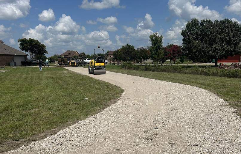 Crew using a heavy roller to compact an asphalt milling and crushed aggregate driveway on a residential property
