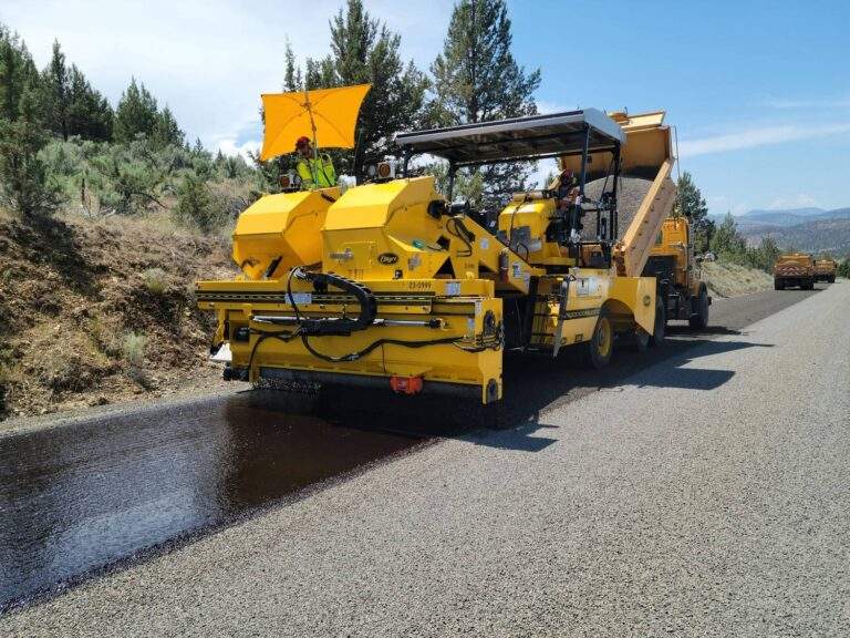 Crew operating heavy chip seal machinery and asphalt paving equipment during a road resurfacing project in North Texas.