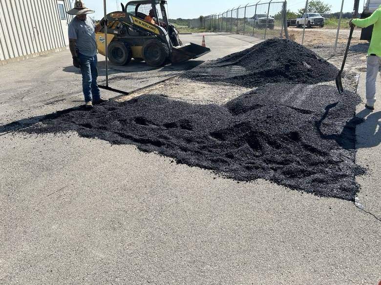 PMG Paving crew members using hand tools and a skid steer loader to spread asphalt milling for commercial pavement repair in North Texas.