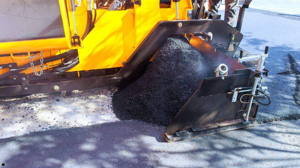 Hot-mix asphalt aggregate being discharged into a paving machine screed during fall commercial parking lot resurfacing